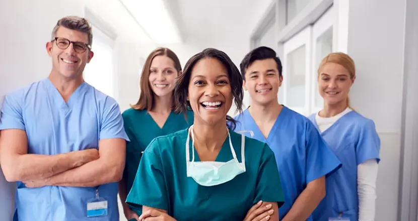 Smiling healthcare professionals in scrubs stand together in a bright, modern medical setting, symbolizing teamwork and dedication in healthcare.